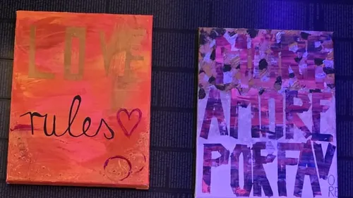 Two colorful canvases with text on a dark wall.