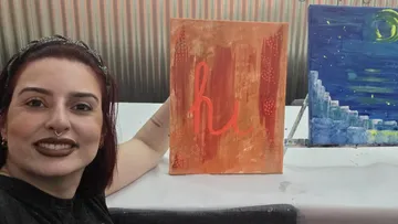 Woman smiling, holding a painting saying 'hi!'.