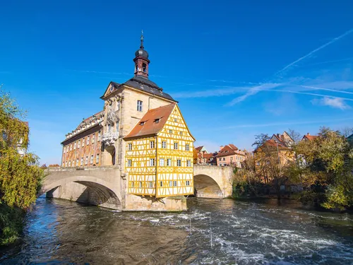 A half-timbered house stands on a river with a bridge.