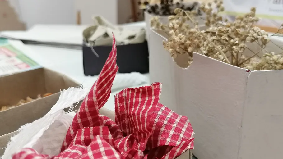 Roter Stoff in Box, getrocknete Blumen daneben.