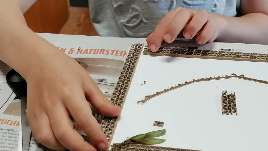 Child crafting with cardboard and leaves indoors.