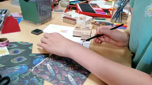 Person zeichnet auf einem überfüllten Kunsttisch.