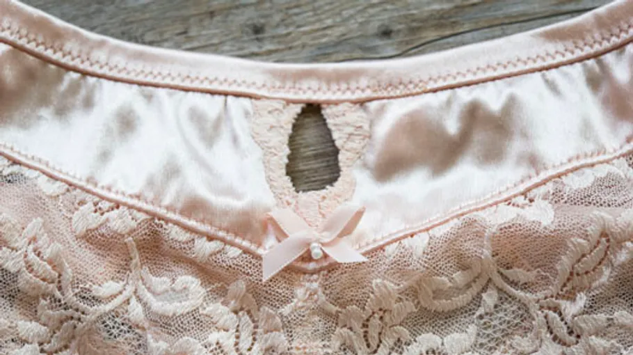 Pink lace garment with bow on wooden surface.