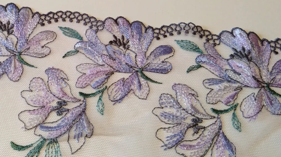 Embroidered purple flowers on lace fabric.