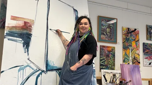 Artist painting on large canvas in gallery.
