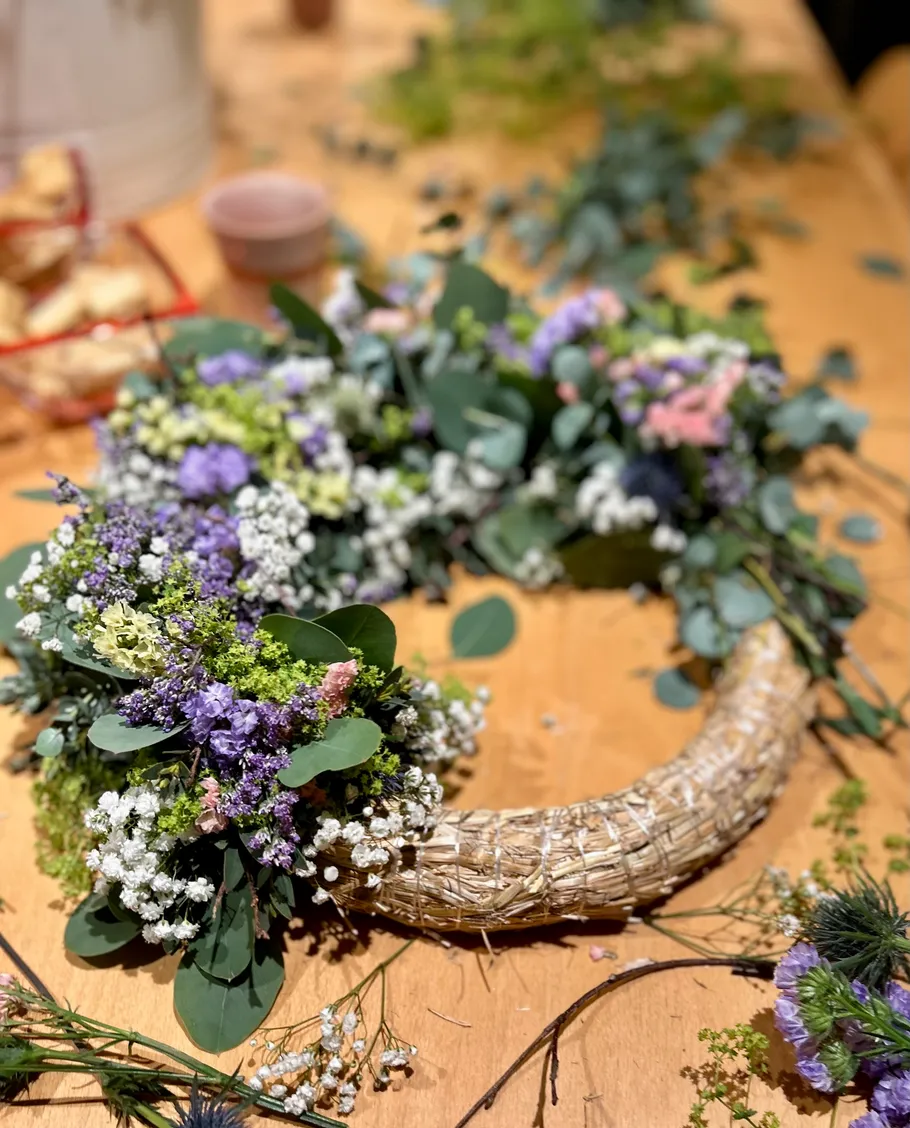 Floral wreath in progress on wooden table.