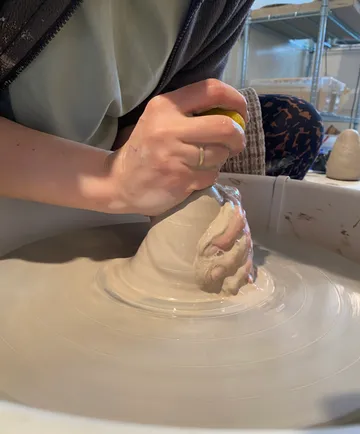 Hands shaping clay on a pottery wheel.