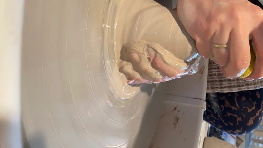 Hand shaping clay on a pottery wheel.