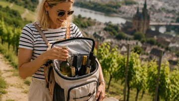 Frau mit Rucksack hält Weinflaschen im Weinberg.