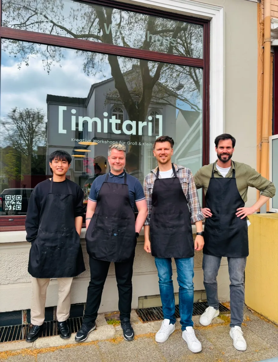 Four people wearing aprons outside workshop.