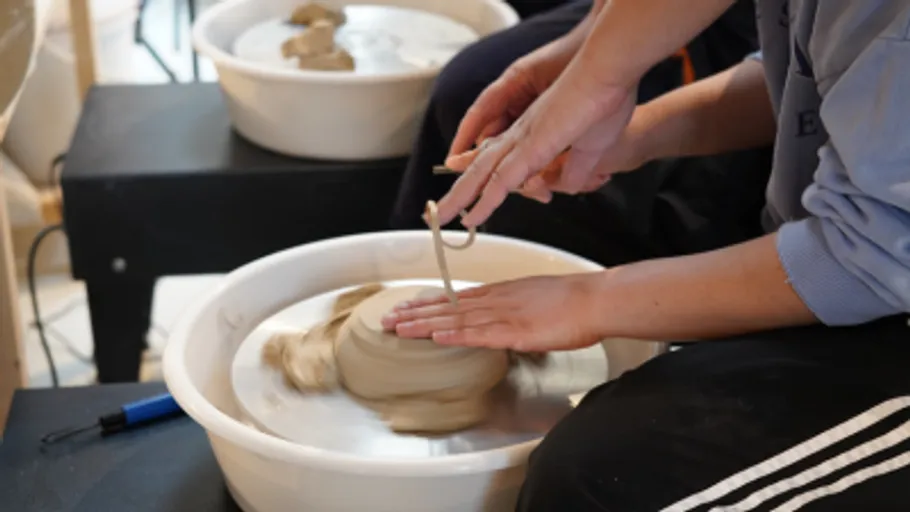 Hands shaping clay on pottery wheel indoors.
