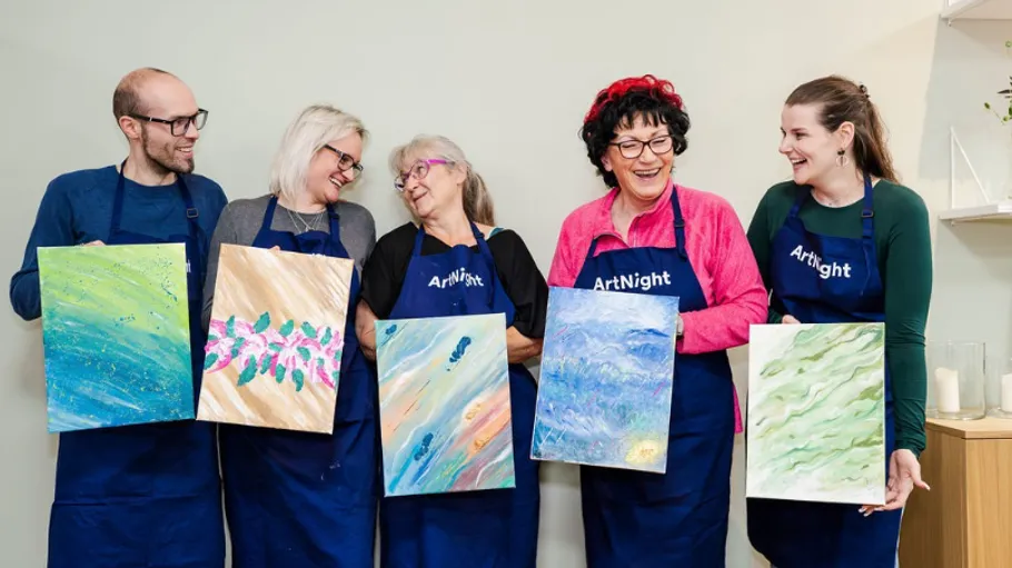 Five people proudly displaying their paintings indoors.