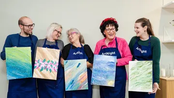 Five people holding painted canvases, smiling indoors.