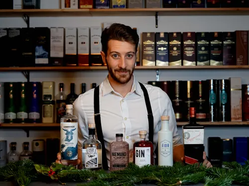 Bartender stands in front of a bar with various bottles.