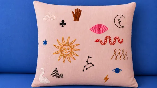 Embroidery symbols on pink cushion, blue background.