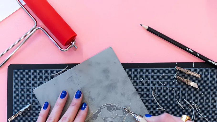Hands carving linoleum on pink background.
