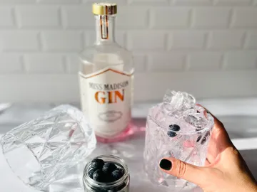 Gin bottle, glass with ice and blueberries in hand.