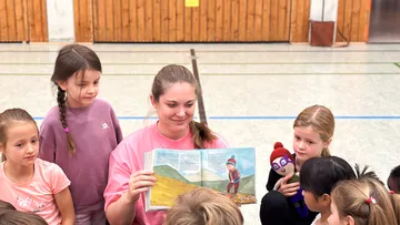 Frau liest Kindern in der Turnhalle vor.