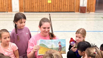 Frau liest Kindern drinnen ein Buch vor.