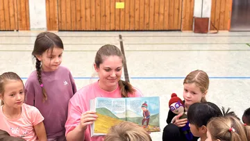 Woman reading book to children, gym setting.