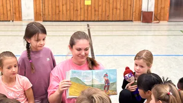 Frau liest Kindern aufmerksam in Innenraum vor.