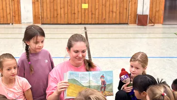 Frau liest interessierten Kindern drinnen ein Buch vor.