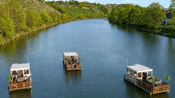 Drei schwimmende Plattformen mit Menschen auf einem Fluss.