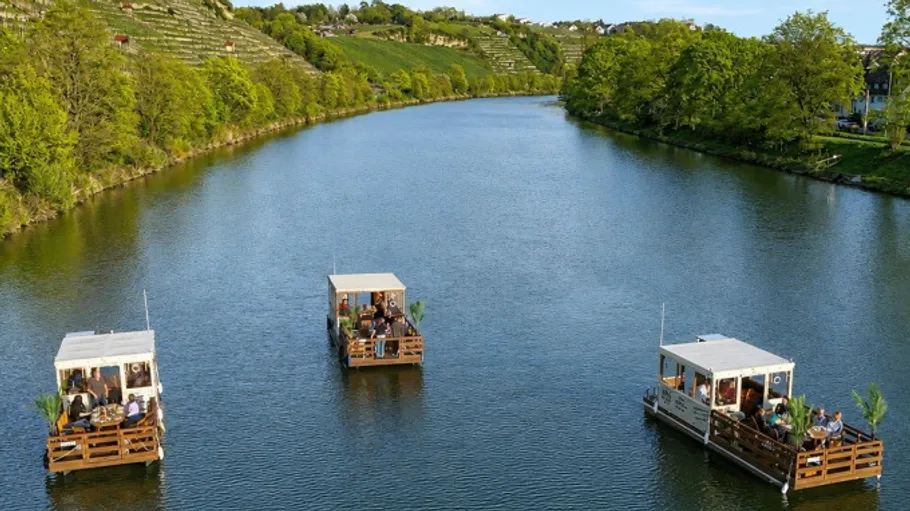 Drei schwimmende Plattformen mit Menschen auf einem Fluss.