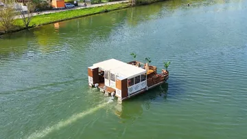 Floating houseboat travels on a river.