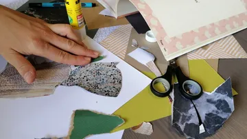 Hand arranging paper scraps on craft table.