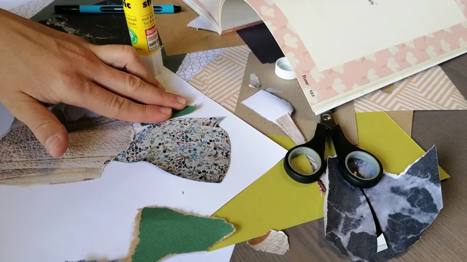 Hand arranging paper scraps on craft table.