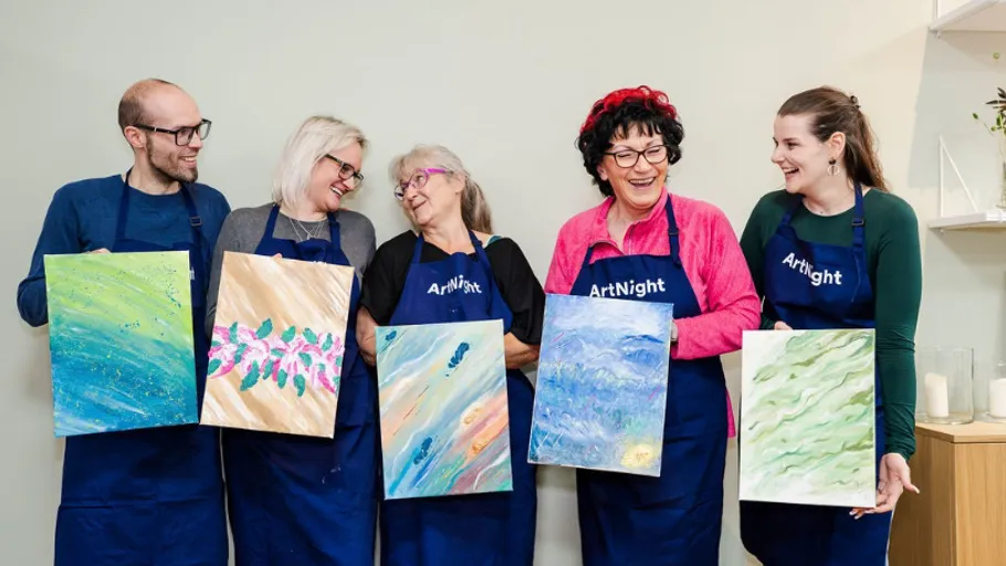 Five people holding paintings, wearing aprons, indoors.