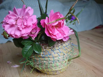 Bouquet of flowers in basket stands on wooden floor.