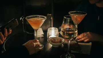 Two cocktails and hands in dimly lit bar.