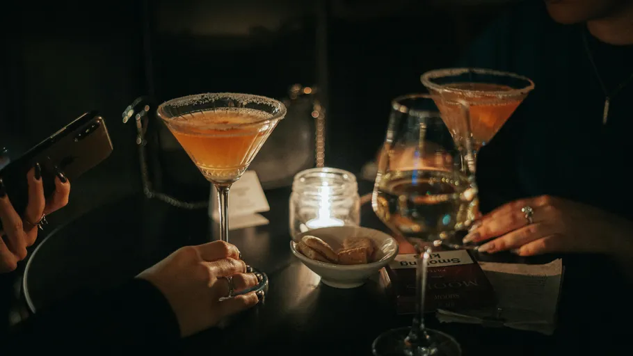 Two cocktails and hands in dimly lit bar.