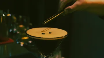 Espresso martini being garnished in a bar.
