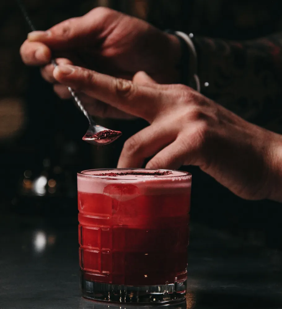 Hand sprinkles red powder on cocktail glass.