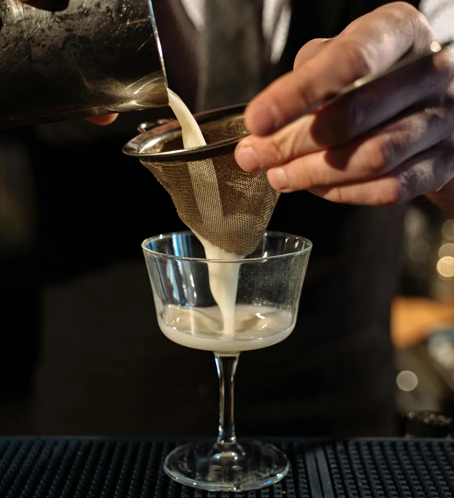 Bartender straining cocktail into glass at bar.