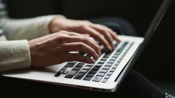 Person typing on laptop in dim light.