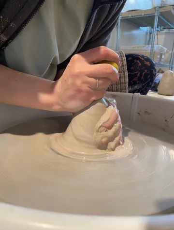 Hand molding clay on spinning pottery wheel.