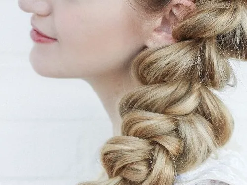 A woman is wearing a braid, side view, against a light background.