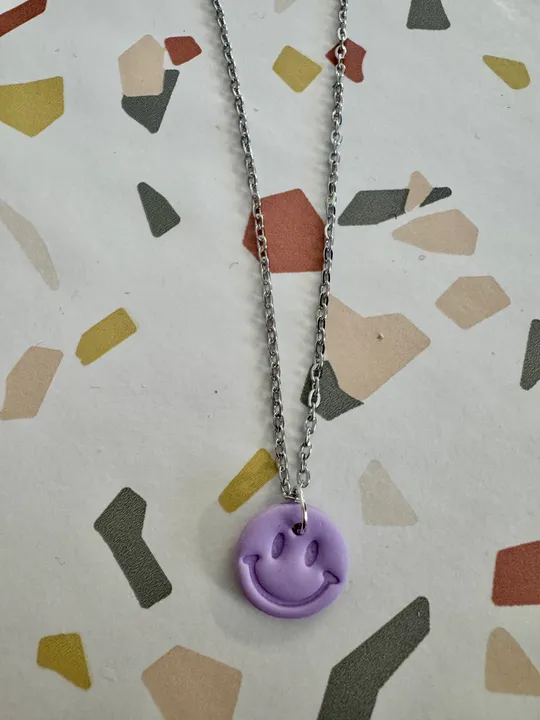 Lila Smiley-Anhänger an Silberkette, geometrischer Hintergrund.