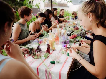 Women create floral arrangements at an outdoor table.