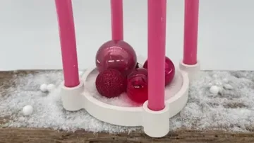Pink candleholder with red ornaments on snow.