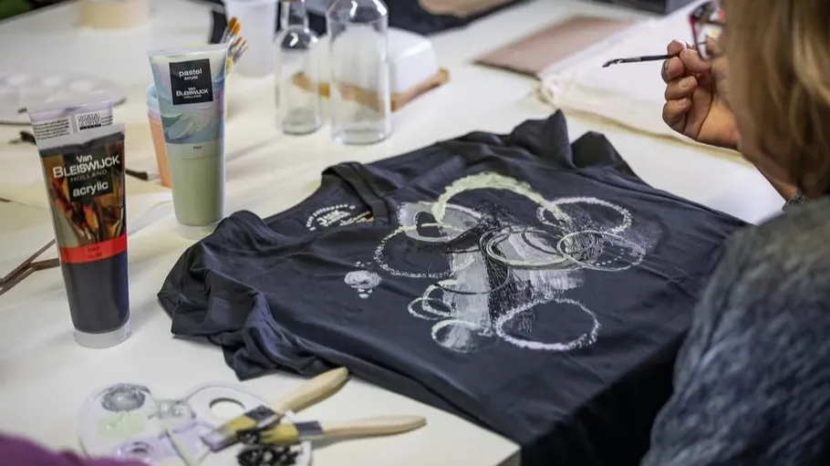 Person painting abstract design on black T-shirt.