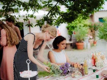 Two women decorate an outdoor table with flowers.