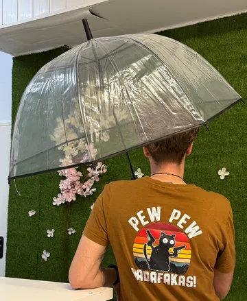 Person holding clear umbrella, wearing cat graphic shirt.