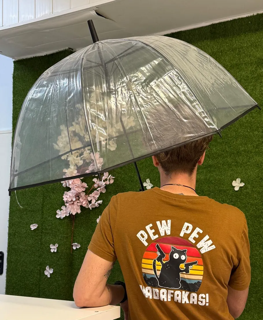 Person hält klaren Regenschirm, trägt Katzenshirt.