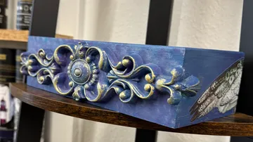 Ornamentales Holzstück mit blauen und goldenen Akzenten.
