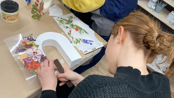 Person decorating letter with floral designs.